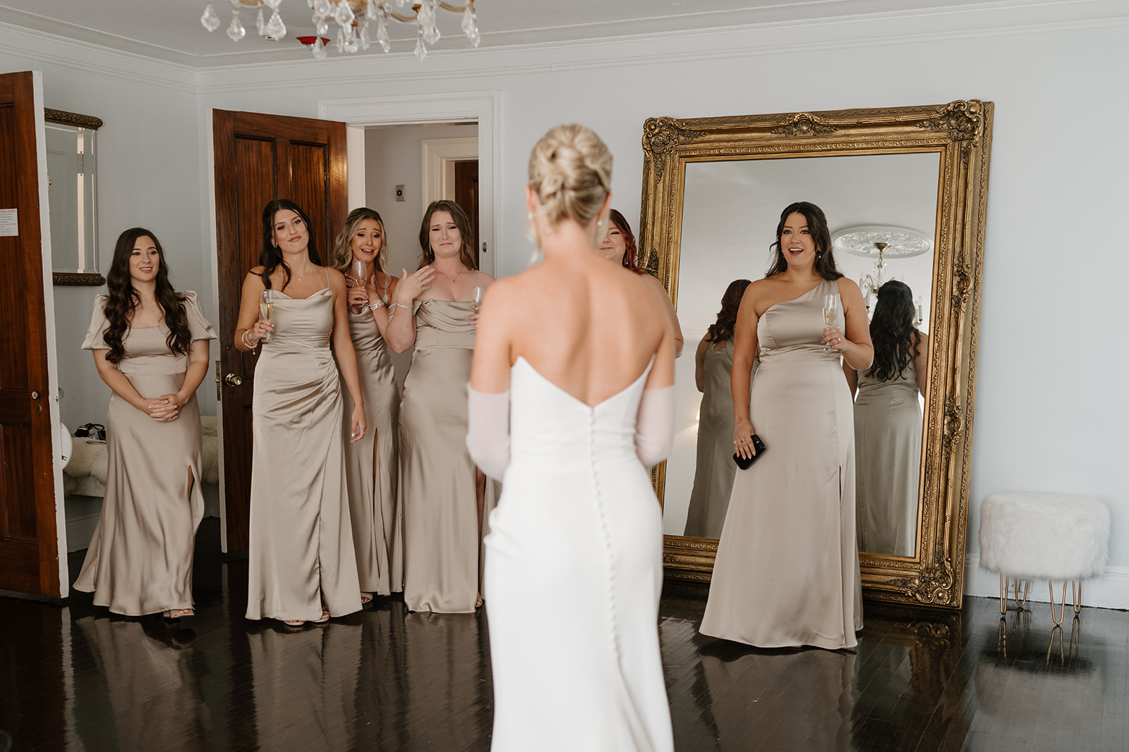 Bridesmaids in champagne gowns tear up and gasp during a first look with the bride in the suite.